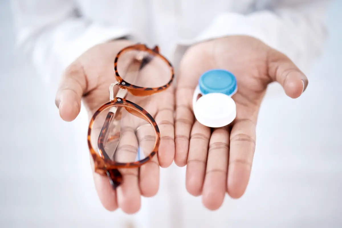 An open pair of hands holding eyeglasses and a contact lens case.
